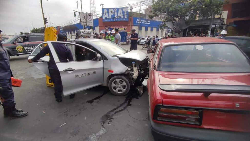 Un auto de color plomo tiene la parte delantera averiada y a su lado un automóvil de color rojo. Ambos vehículos sufrieron un accidente de tránsito